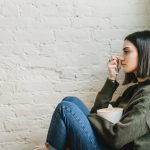 thoughtful young ethnic woman crying near brick wall at home